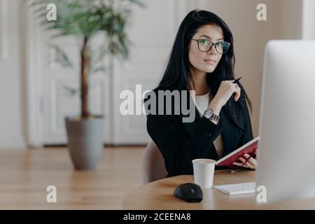 Foto von serious Frau schreibt Informationen in Notebook, Studien neue Online-Business-Kurs, Posen in Coworking Space mit Computer, arbeitet an Projekt, w Stockfoto