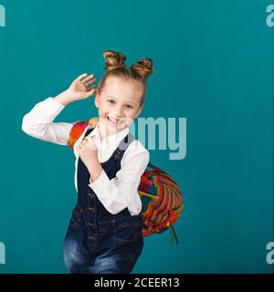 Lustige lächelnde kleine Mädchen mit großen Rucksack springen und Spaß an der blauen Wand. Blick auf die Kamera. Schulkonzept. Zurück zur Schule Stockfoto