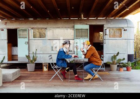Junger Mann und Frau genießen leckeren Kuchen, während sie am Tisch in der Nähe von grungy van sitzen Stockfoto