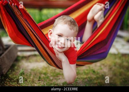 Schöner fröhlicher kleiner Junge, der in einer Hängematte ruht und Spaß hat. Positive Emotionen. Stockfoto