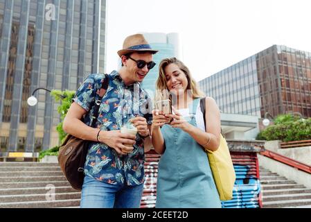 Fröhlicher junger Mann und Frau, die auf der Straße stehen und das Smartphone an einer Treppe benutzen Stockfoto