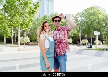 Fröhlicher junger Mann und Frau, die im sonnigen Park in der Stadt stehen Stockfoto