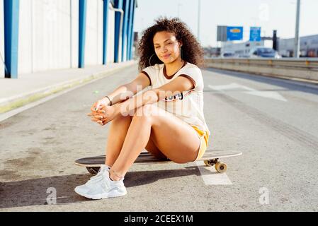 Afroamerikanischer Teenager sitzt auf dem Skateboard auf der Straße Stockfoto