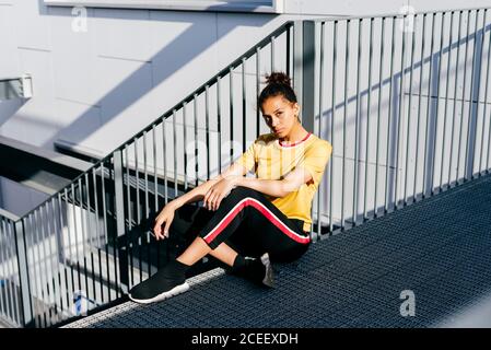 Attraktive junge ethnische Frau in Sportkleidung, die auf Treppen sitzt und die Kamera anschaut. Stockfoto