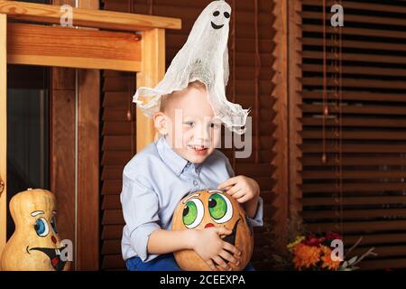 Niedlicher kleiner Junge mit Spaß in Halloween-Dekorationen. Halloween-Party mit Kind hält bemalten Kürbis Stockfoto