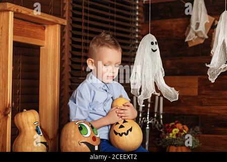 Niedlicher kleiner Junge mit Spaß in Halloween-Dekorationen. Halloween-Party mit Kind hält bemalten Kürbis Stockfoto