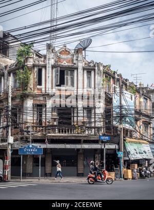 Bangkok, Thailand, Südostasien - zwei Personen auf dem Motorrad und eine Dame zu Fuß vor dem alten Gebäude. Komplizierte Stromkabel. Stockfoto