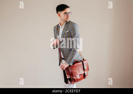 Seitenansicht des stylischen jungen Mannes in Brille und lässiger Jacke stehend und rückblickend. Stockfoto