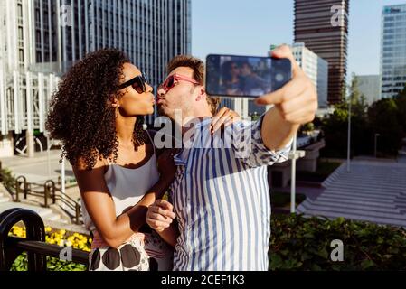 Schöne schwarze Frau und hübscher kaukasischer Mann posieren für Selfie, während sie auf dem Hintergrund der modernen Stadt stehen Stockfoto