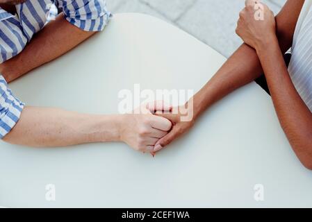 Von oben Schuss von unkenntlich multirassischen Paar Hände halten, während Gemeinsam am Tisch im Café im Freien sitzen Stockfoto