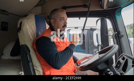 Männlicher Mechaniker in einer orangefarbenen Weste, der auf dem Fahrer sitzt Sitz eines Staplers Stockfoto