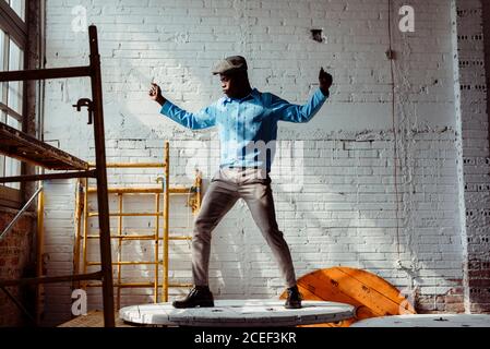 Attraktiver afroamerikanischer Mann im lässigen Outfit, der auf dem runden Tisch tanzt In stilvollem, hellem Loft Stockfoto