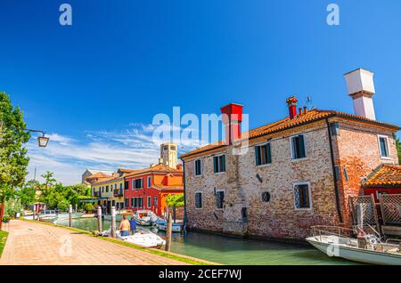 Insel Torcello mit Uferpromenade entlang des Wasserkanals mit Motorbooten und bunten Gebäuden. Turm und blauer Himmel Hintergrund. Lagune Von Venedig, Region Venetien, Norditalien. Stockfoto