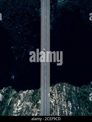 Luftaufnahme von Kleinwagen fahren auf leerer Straße von Brücke über dunkles Meer Bucht Wasser mit felsigen Küste Stockfoto
