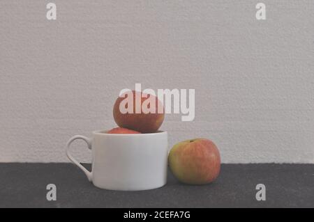 Äpfel. In weißer Keramik-Kaffeetasse, mit einem isolierten Apfel, der das Konzept der Trennung, Diskriminierung, Konzeptfoto, weißer Hintergrund, Braz Stockfoto