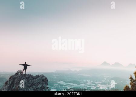 Rückansicht einer jungen Frau mit ausgestreckten Armen, die auf dem Berg stehen und die Aussicht bewundern Stockfoto