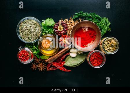 Von oben Satz von verschiedenen Gewürzen und Kräutern auf schwarzen Hintergrund platziert um eine Flasche Öl Stockfoto