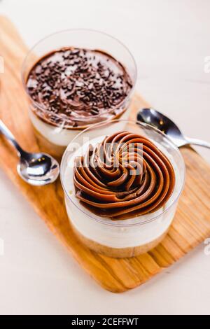 Nahaufnahme von süßen Desserts in einer Tasse gefüllt mit Sahne und serviert mit Löffeln auf Holzbrett. Stockfoto