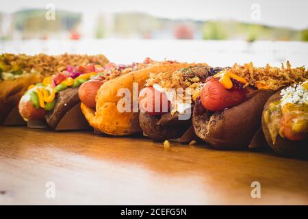 Reihe von verschiedenen Hot Dogs mit verschiedenen leckeren Toppings und Füllungen auf Holzbrett. Stockfoto