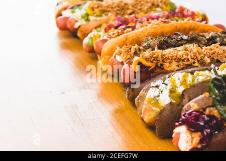 Reihe von verschiedenen Hot Dogs mit verschiedenen leckeren Toppings und Füllungen auf Holzbrett. Stockfoto