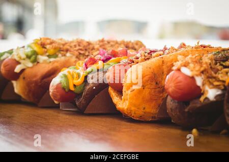 Reihe von verschiedenen Hot Dogs mit verschiedenen leckeren Toppings und Füllungen auf Holzbrett. Stockfoto