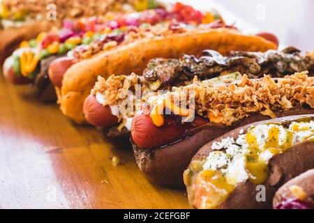 Reihe von verschiedenen Hot Dogs mit verschiedenen leckeren Toppings und Füllungen auf Holzbrett. Stockfoto