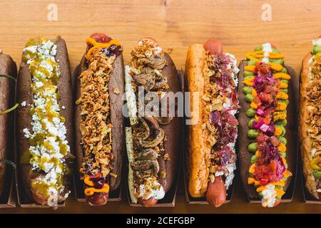 Reihe von verschiedenen Hot Dogs mit verschiedenen leckeren Toppings und Füllungen auf Holzbrett. Stockfoto