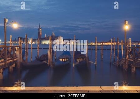 Drei leere Gondeln, die an Holzpfählen am ruhigen Kanal befestigt sind Wasser in bewölktem Abend im erstaunlichen Venedig Stockfoto