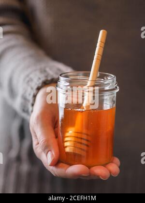 Nahaufnahme der Hand der anonymen Frau, die ein kleines Glas frischen Honigs mit Löffel hält Stockfoto