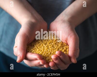 Nahaufnahme der Ptim Pasta in weiblichen Händen. Ptitim oder Couscous ist traditionelles israelisches Essen. Trockenes oder rohes Ptitim mit Kopierraum für Text. Stockfoto