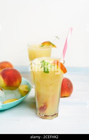 Pfirsich erfrischender Saftcocktail im Glas mit Eis und Fruchtstücken und Minze im Sommer. Draufsicht auf hellem Hintergrund. Stockfoto