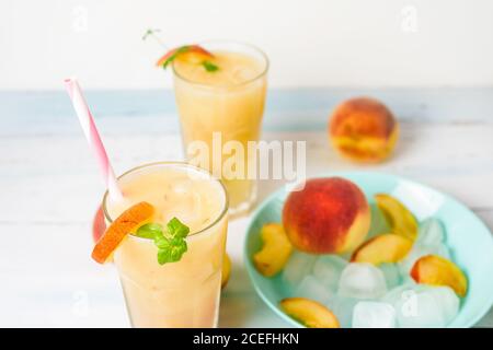 Pfirsich erfrischender Saftcocktail im Glas mit Eis und Fruchtstücken und Minze im Sommer. Draufsicht auf hellem Hintergrund. Stockfoto