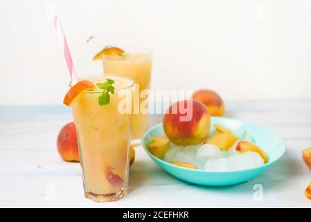 Pfirsich erfrischender Saftcocktail im Glas mit Eis und Fruchtstücken und Minze im Sommer. Draufsicht auf hellem Hintergrund. Stockfoto