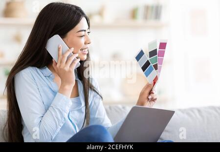 Lächelnde Asiatische Frau Holding Farbpalette, Im Gespräch Auf Handy Mit Interior Designer Stockfoto