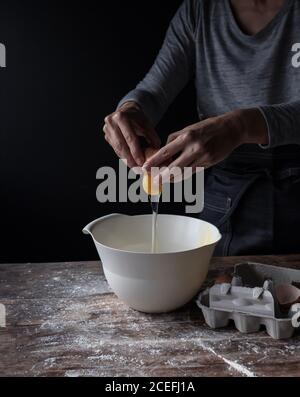 Erntegut, das Ei in die Schüssel auf hölzernen Tisch mit Mehl auf schwarzem Hintergrund Stockfoto