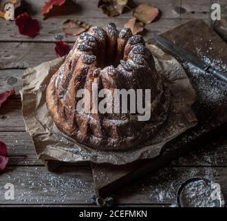 Frisch schmackhafter Kugelhopf auf Pergamentpapier auf verwittertem Holz stehend Tischplatte in der Nähe von trockenen Herbstblättern Stockfoto