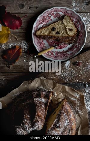 Zarte Herbstblätter liegen auf schäbiger Holzplatte in der Nähe der Platte Und Pergamentpapier mit leckeren frischen Kugelhopf Stockfoto