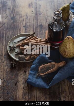 Von oben Schuss der reifen Birnen, die neben der Flasche liegen Rotwein und Teller mit verschiedenen aromatischen Gewürzen auf Holz Tischplatte Stockfoto