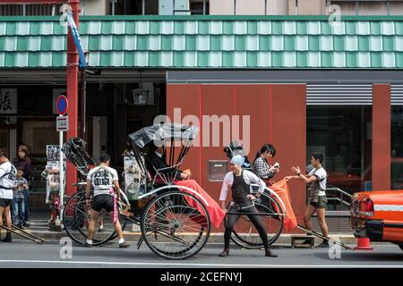 Asakusa, Tokio, Japan - Rickshaw-Fahrer und Kunden auf der Straße in der Nähe von Sensō-ji, dem ältesten Tempel in Tokio. Attraktion für Touristen. Stockfoto