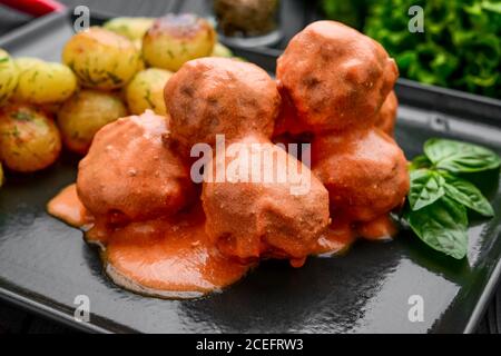 Fleischbällchen in Tomate, mit gekochten Kartoffeln auf einem schwarzen Teller Stockfoto
