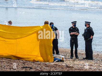 Polizei bei einem Vorfall an einem Strand in England, Großbritannien, mit einem Bildschirm für die Privatsphäre & Offiziere tragen Gesichtsmasken wegen der COVID19 Coronavirus Pandemie. Stockfoto