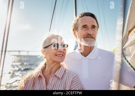 Porträt von zwei älteren Menschen, die wegschauen. Reifes Paar, das auf der Yacht steht und ihren Segeltörn genießt. Stockfoto