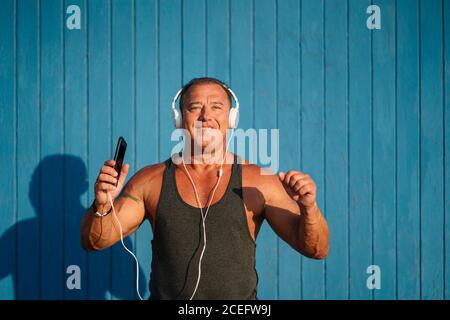 Starker älterer Mann posiert mit Kopfhörern auf blauem Hintergrund. Stockfoto