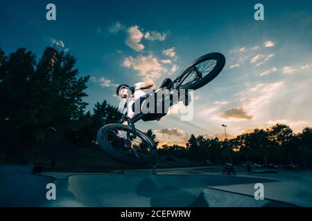 Junger Sportler macht Tricks auf BMX im Park auf Hintergrund Von blauem bewölktem Himmel Stockfoto