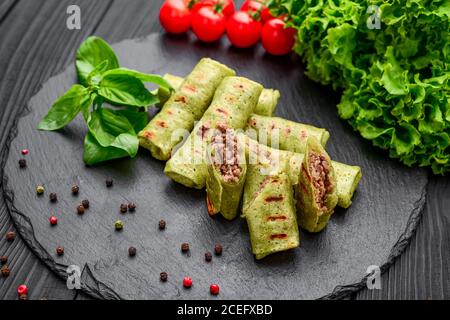 Dünne Pfannkuchen mit Spinat und Fleisch auf schwarzem Hintergrund Stockfoto