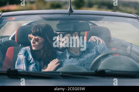 Brünette Frau in legerer Kleidung und bärtigen Mann im Hemd sitzen in dunklen Auto und wegschauen Stockfoto