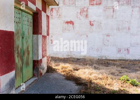 Alte Metalltür und verblasste rot-weiß karierte Wand, alles veraltet, aus einer ehemaligen mechanischen Werkstatt. Stockfoto