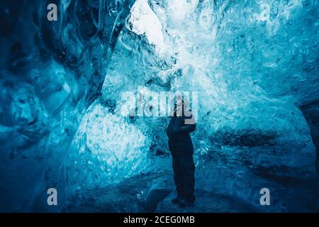 Reisender Mann im Äußern stehend in kristallblauer Eishöhle, der nach oben schaut, Island Stockfoto