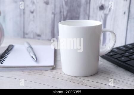 Weißer Becher Mockup mit Tastatur, Notizbücher auf Tisch Stockfoto