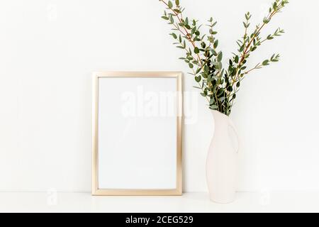 Blanker Rahmen Mockup mit einem Zweige von Eukalyptus in Vase auf Tisch auf hellem Hintergrund. Inneneinrichtung. Blog, Website oder Social Media Konzept. Stockfoto